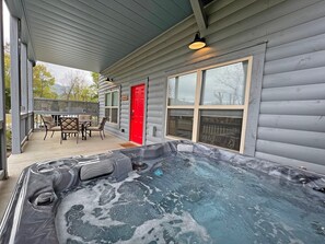 A hot tub outside a cabin with a covered patio, a red door, and a table with chairs. - Love Shack Cozy, Affordable Cabin in Downtown Bryson City (Bryson City)