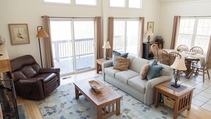 A spacious living area with a sofa, a coffee table, a brown leather chair, a dining table with chairs, and a balcony with curtains. - Hidden Mountain Retreat Absolute Seclusion near Cherokee (Whittier)