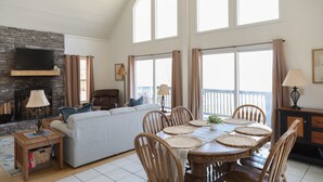 A living room with a fireplace, a sofa, a dining table with chairs, and large windows. - Hidden Mountain Retreat Absolute Seclusion near Cherokee (Whittier)