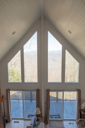 A room with large windows, a wooden deck, and a view of trees and mountains.