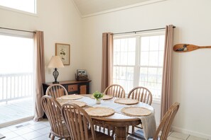 A dining area with a round table, six chairs, a vase with flowers, a lamp, a wooden paddle on the wall, and a window with curtains. - Hidden Mountain Retreat Absolute Seclusion near Cherokee (Whittier)