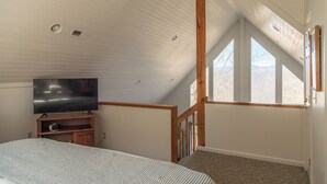 A bedroom with a TV on a wooden stand, a bed with a striped bedspread, and a large window with a view of the outdoors. - Hidden Mountain Retreat Absolute Seclusion near Cherokee (Whittier)
