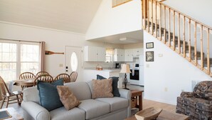 A living room with a sofa, a wooden coffee table, a patterned armchair, a dining table with chairs, and a kitchen in the background. - Hidden Mountain Retreat Absolute Seclusion near Cherokee (Whittier)