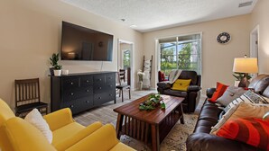 A living room with a flat-screen TV, a wooden coffee table, a yellow sofa, a brown leather couch, and a black entertainment unit. - Pet friendly Pool Home with King suite 10 minutes to Disney World (Davenport)