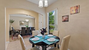 A dining area with a round table set for four, surrounded by chairs, with a vase of flowers on the table. - Pet friendly Pool Home with King suite 10 minutes to Disney World (Davenport)