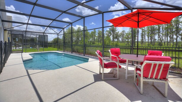 A covered outdoor area with a pool, red chairs, and a table. - Pet friendly Pool Home with King suite 10 minutes to Disney World (Davenport)
