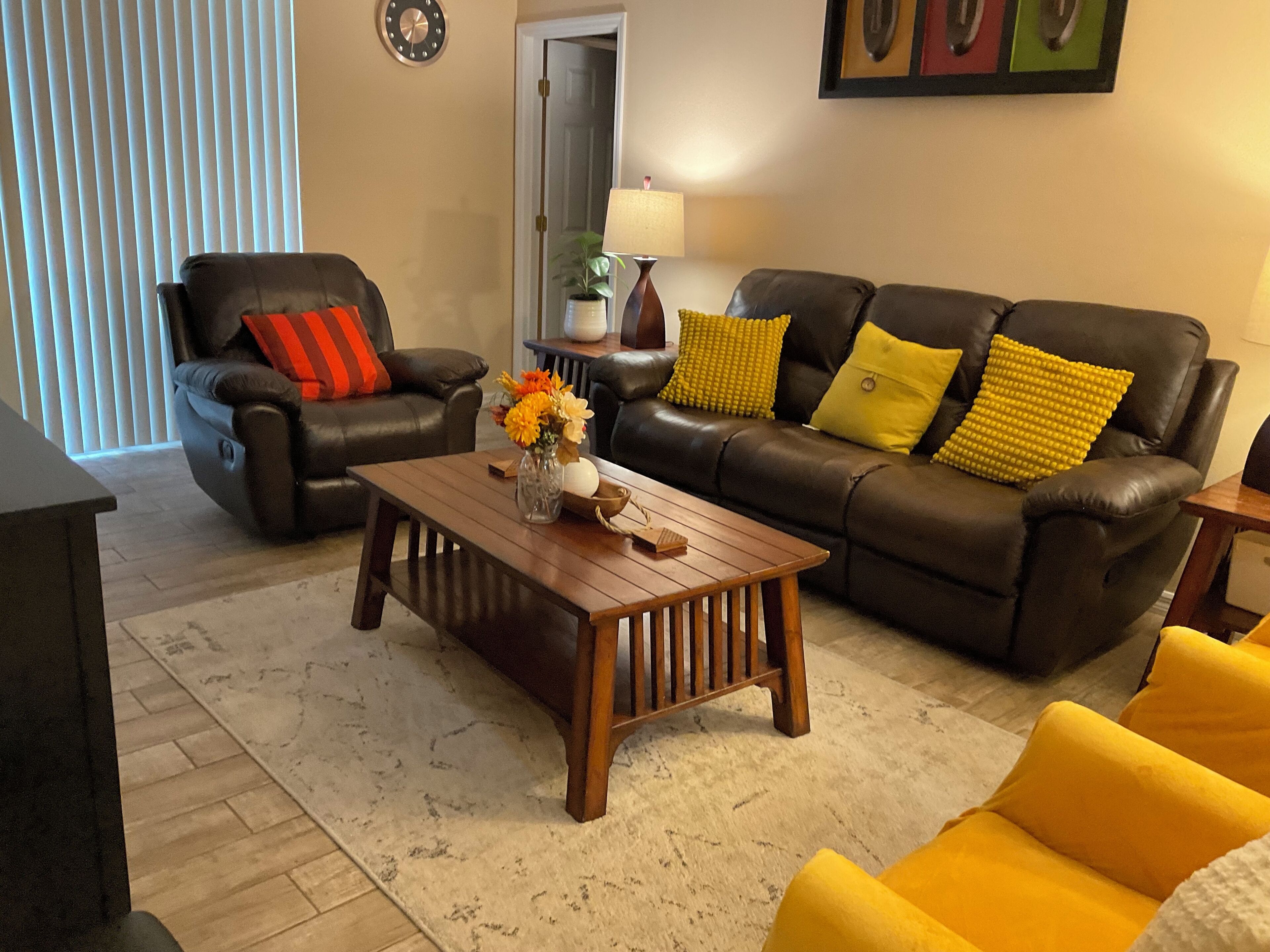 A living room with a brown leather sofa, a wooden coffee table, and a yellow armchair.