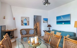 A living room with a glass coffee table, wicker furniture, a fireplace, and coastal-themed artwork.