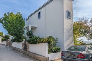A modern two-story building with a white facade, a stone base, and a car parked in front.