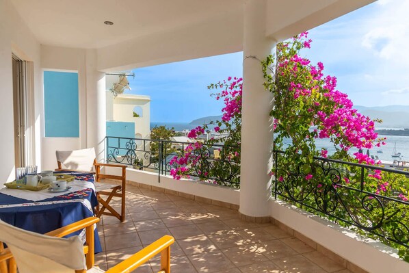 A balcony with a table set for breakfast, a chair, and a view of the sea and mountains.