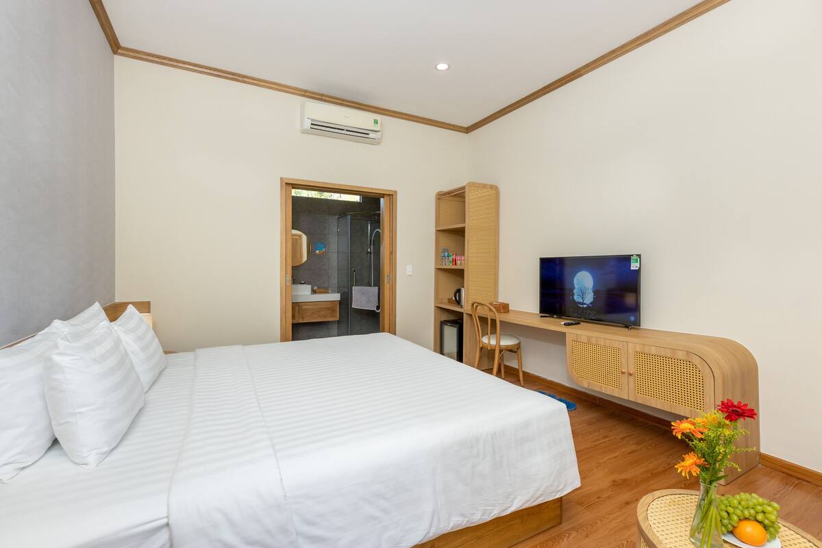 Hotellihuone, jossa on sänky, televisio, työpöytä ja kylpyhuone, ja kaikki näkyy avoimesta ovesta.