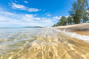 Una playa con agua cristalina, orilla de arena y árboles al fondo.