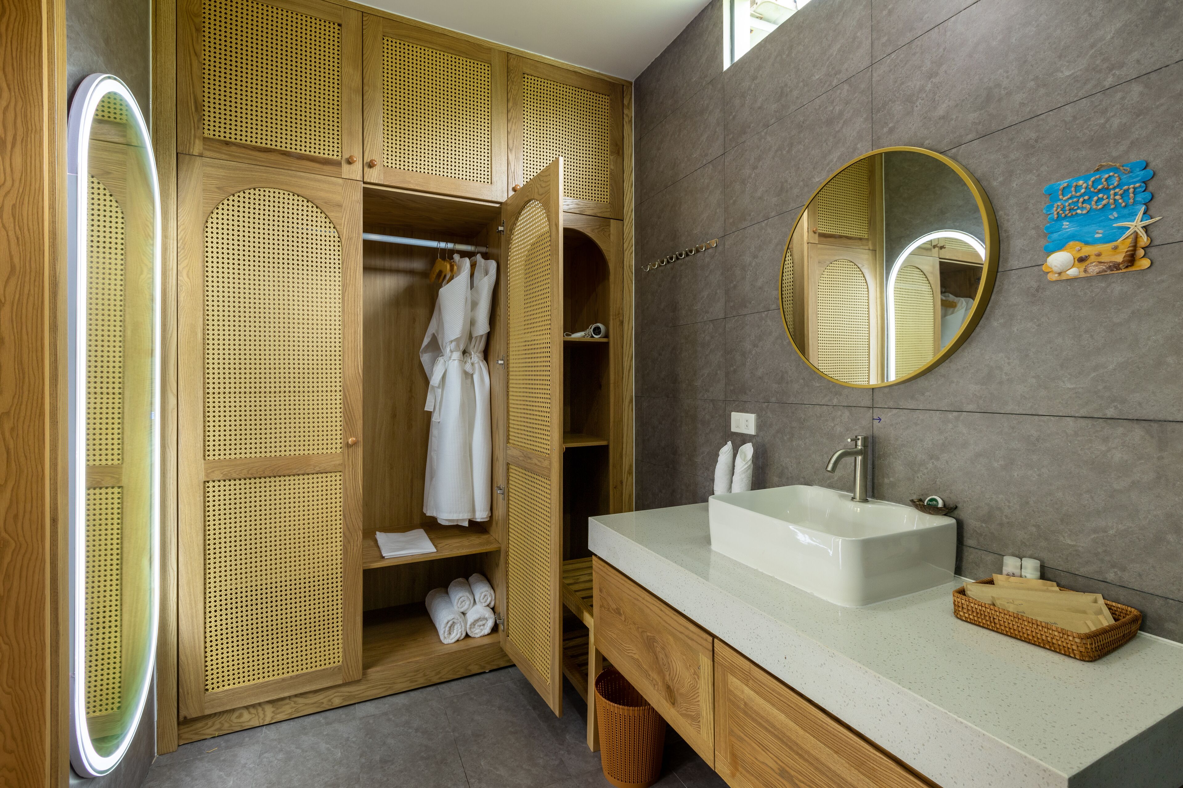 A modern bathroom with a wooden vanity, a large mirror, and a sign indicating a 'TOCO RESORT'.