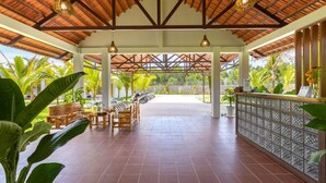 A covered outdoor seating area with a tiled floor, wooden furniture, and a view of the surrounding greenery. - Coco Garden Resort Phu Quoc (Phu Quoc)