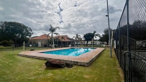 A rectangular swimming pool with a brick border, surrounded by a grassy area and a chain-link fence. - Goin Coastal  Cabin 94 Geographe Holiday Park (Busselton)