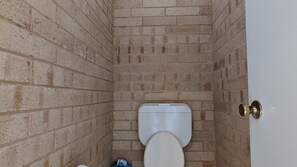 Une petite salle de bain étroite, avec des toilettes blanches et une porte dotée d’une poignée en laiton.