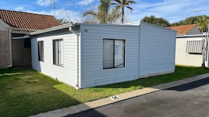 A single-story mobile home with a number '94' on the side, a small front porch, and a clear sky in the background.