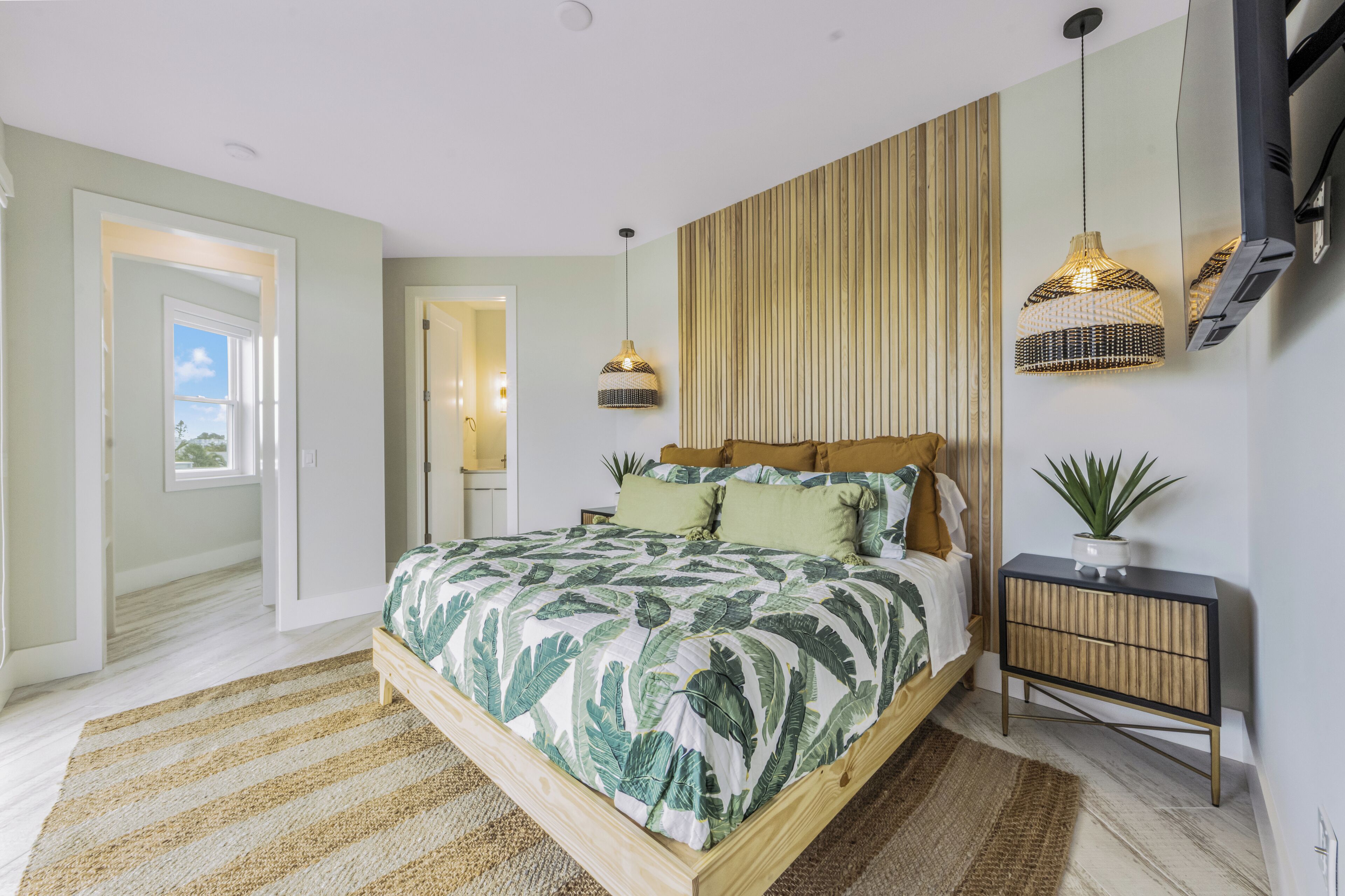 A bedroom with a bed, bedside tables, a hanging light fixture, and a potted plant.