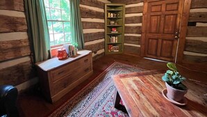 Una camera in una baita di legno, con una scrivania, una libreria, una finestra con tende e una porta.