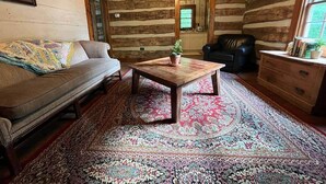 Interno di una baita in legno con un divano, un tavolino da caffè con una pianta, una poltrona in pelle e un comò di legno.