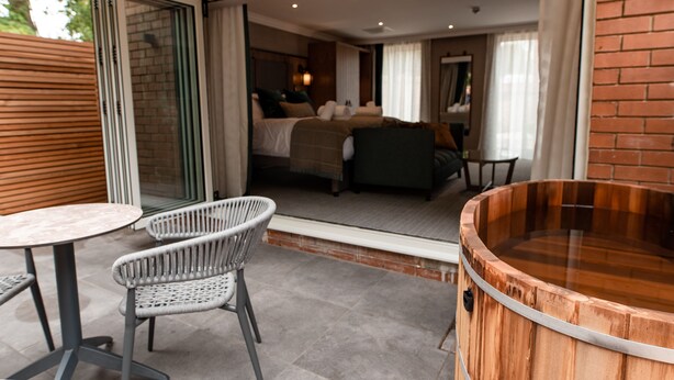 Ein modernes Hotelzimmer mit Glastür zu einem Balkon, einer Holztonne als Whirlpool und Korbmöbeln.
