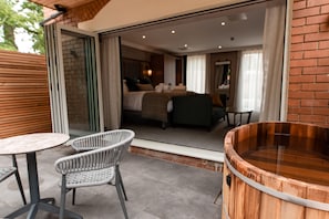 A modern hotel room with a glass door leading to a balcony, a wooden hot tub, and wicker furniture. - Stables Ashbourne (Ashbourne)