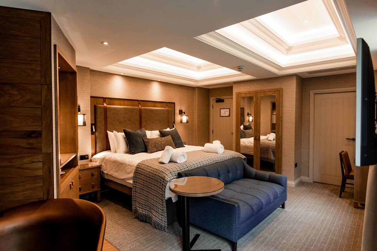 A hotel room with a large bed, a sofa, a small table, and a mirror.