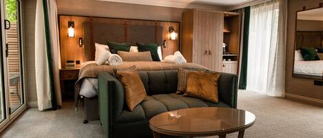 Habitación de hotel moderna con una cama grande, un sofá, una mesa de centro de vidrio y vistas a zonas verdes por la ventana.