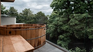 Ein hölzernes Whirlpool auf einem Balkon mit Blick auf dichte Bäume.