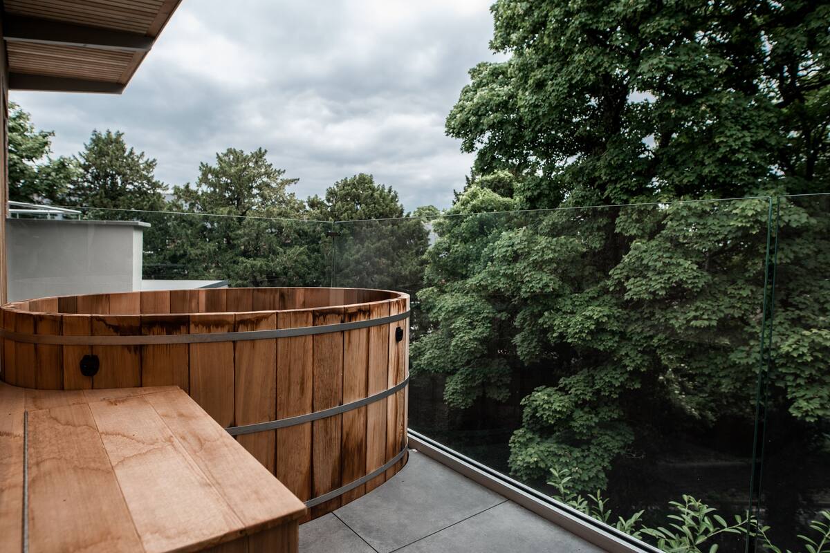 A wooden hot tub on a balcony with a view of dense trees.