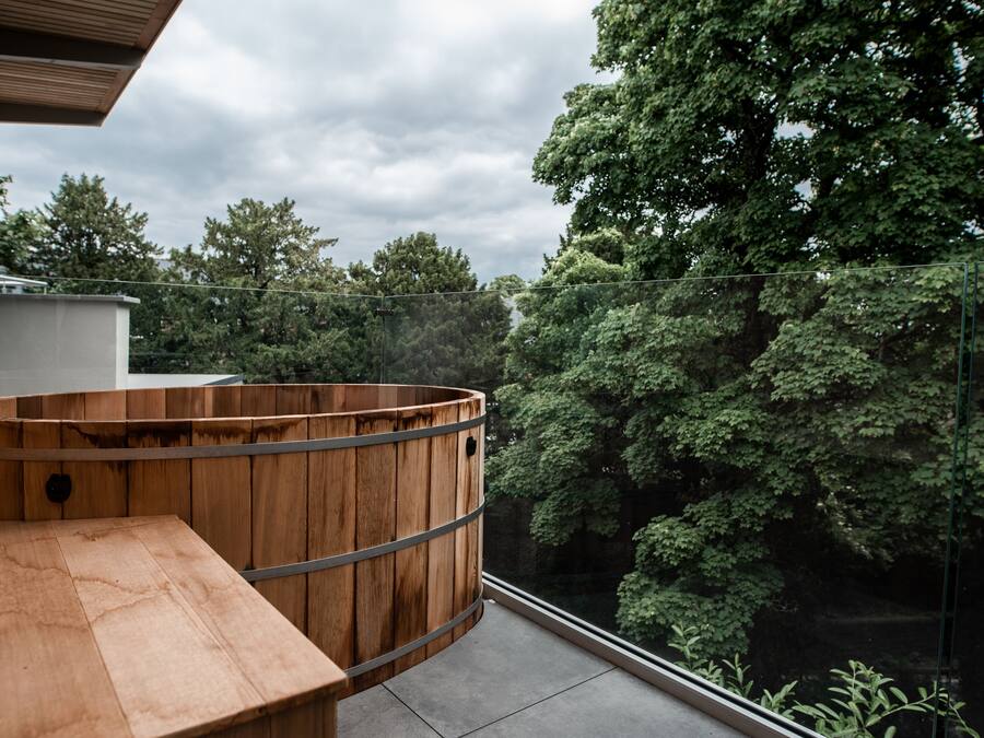 Un bain à remous en bois sur un balcon, avec vue sur une forêt dense.