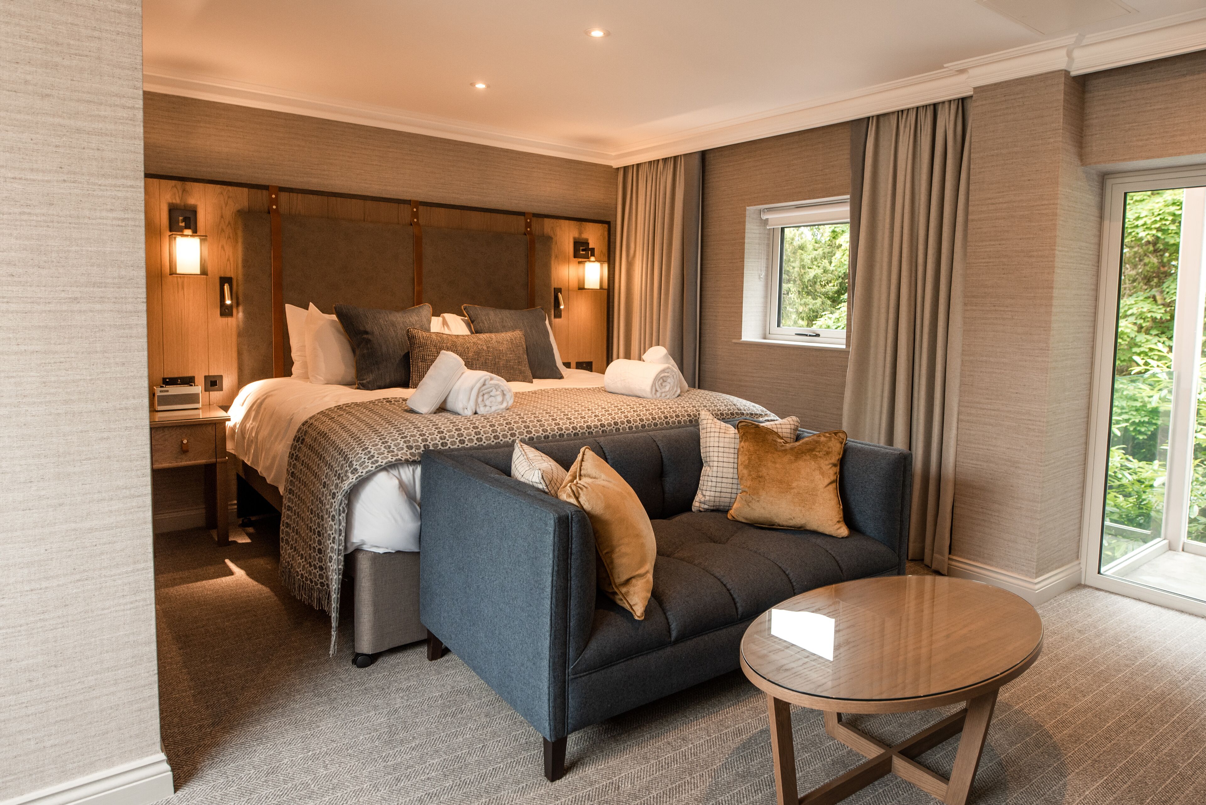 A hotel room with a large bed, a sofa, a small table, and a window with curtains.