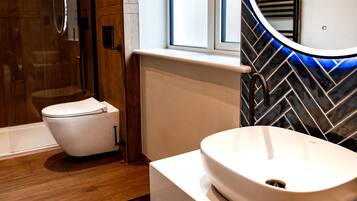 A modern bathroom with a white toilet, a vessel sink, and a mirror with a blue light.