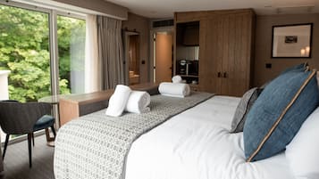 A modern hotel room with a large bed, a desk, and a view of greenery outside.