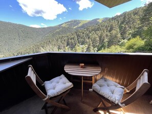 Une terrasse en bois avec deux fauteuils rembourrés et une petite table, offrant une vue sur un paysage montagneux boisé.