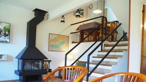A cozy living room with a fireplace, wooden chairs, a dining table, and a staircase. - Apartamento en La Molina, Grandes Vistas, Chimenea (La Molina, Alp)