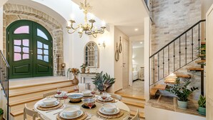Un coin repas avec une table ronde dressée pour six personnes, un escalier et une porte verte.