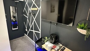Ein modernes Zimmer mit einem schwarz-weißen geometrischen Wanddesign, einem Flachbildfernseher, einer Kaffeestation und einem Spiegel.