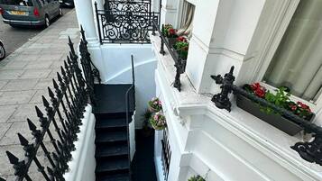 A narrow, white building with black iron railings and a staircase leading to a landing.
