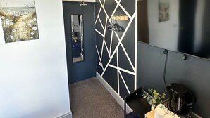 A modern bathroom with a geometric wall design, a mirror, a sink, and a vanity with a clock and decorative items. - Amsterdam Hotel (London)
