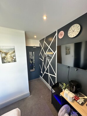 A modern bathroom with a geometric wall design, a mirror, a sink, and a vanity with a clock and decorative items. - Amsterdam Hotel (London)