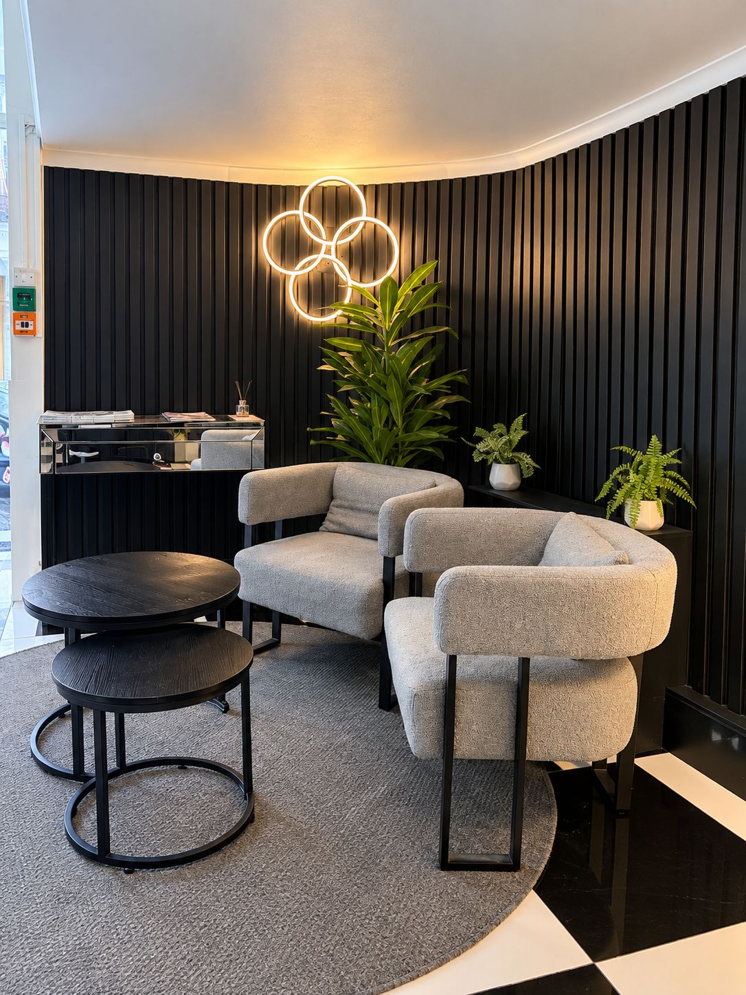 A modern interior with a curved wall, a round table, two grey armchairs, and a potted plant.