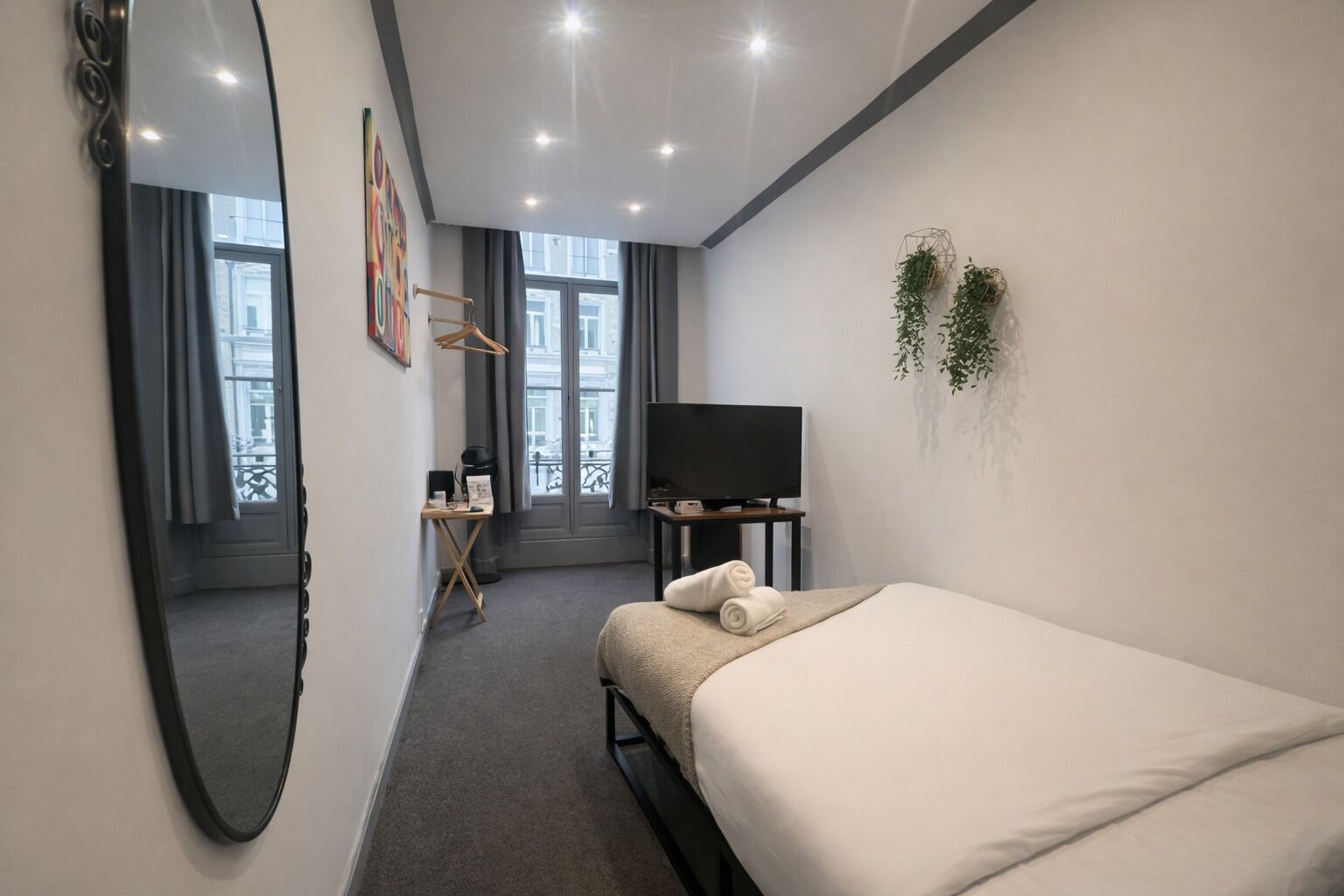 Habitación de hotel con cama, escritorio, silla, televisor y un espejo grande.