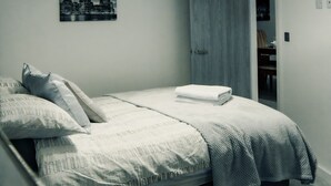 A bedroom with a bed, a cityscape picture on the wall, and a door leading to another room.