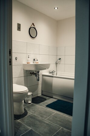Ein modernes Badezimmer mit Waschbecken, Toilette und Badewanne, alles in Weiß.