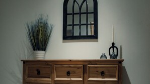 A wooden cabinet with drawers and a glass top, a potted plant, a candle, and a mirror on the wall.