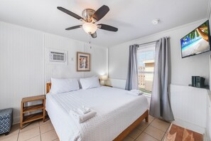 A bedroom with a bed, a ceiling fan, a TV, a window with curtains, and a small table.