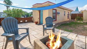 A backyard patio with two Adirondack chairs, a fire pit, and a house with a red door and blue awning. - This attractive cottage at Spanish Village in Port Aransas is a free standing ho (Port Aansas)