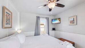A hotel room with a large bed, a ceiling fan, a TV, and a window with curtains. - This attractive cottage at Spanish Village in Port Aransas is a free standing ho (Port Aansas)