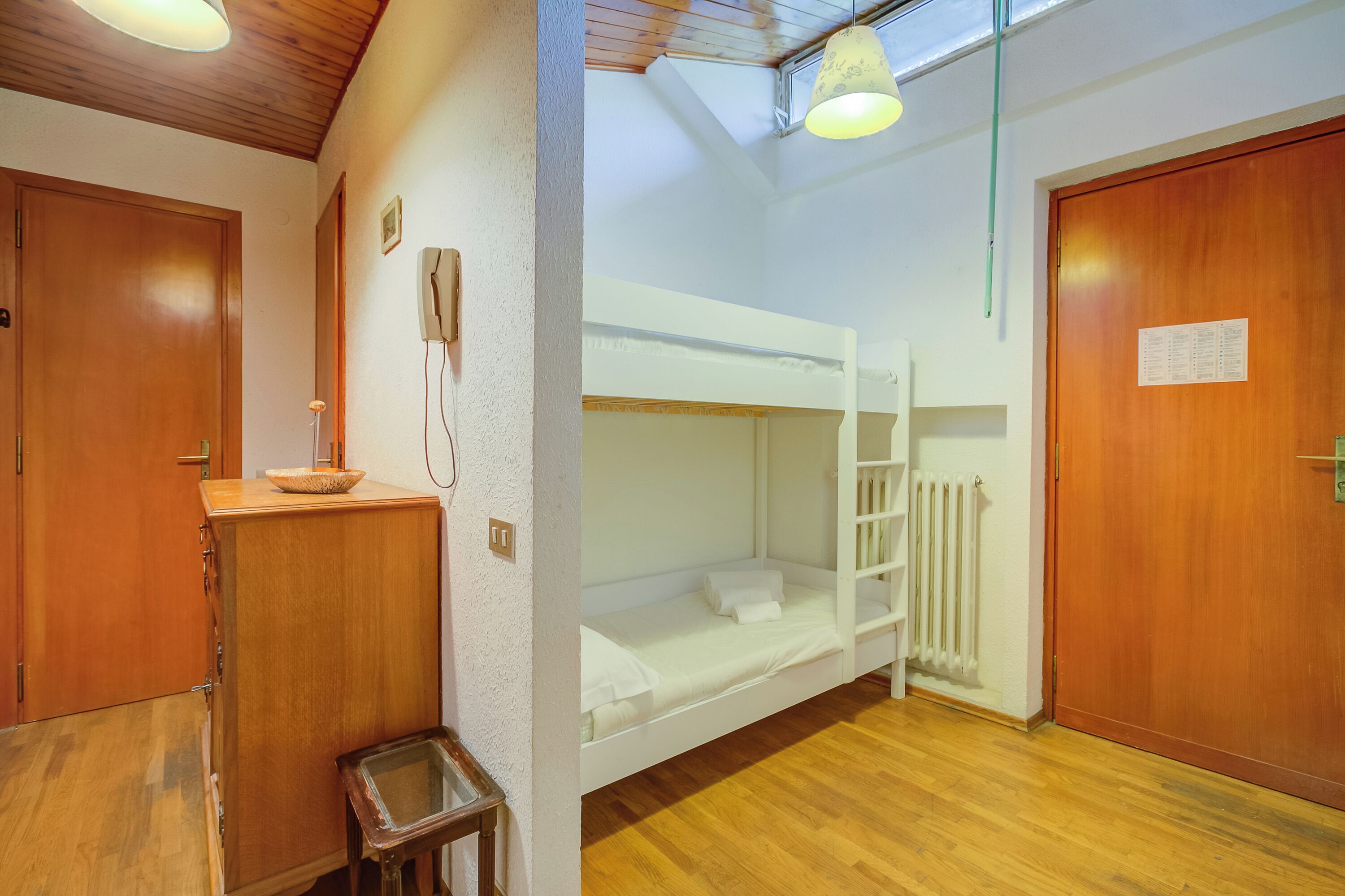 Habitación con literas, un armario de madera, un cubo de basura pequeño y un radiador.